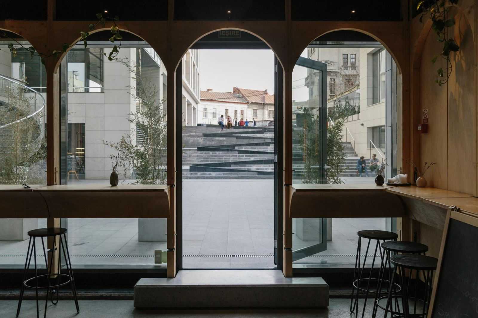 Zona de intrare cu perete vitrat și mese suspendate din placaj cu elemente curbate