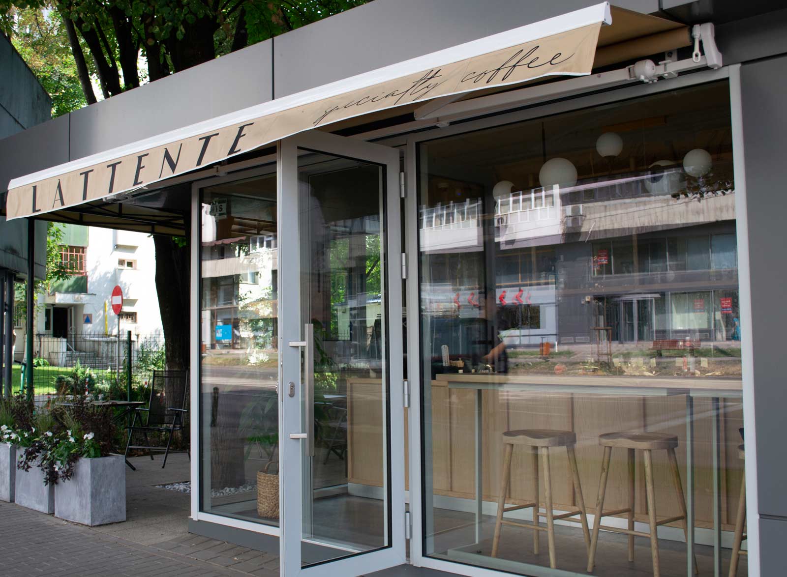 Imagine de ansamblu de afară a cafenelei cu mobilierul de la interior vizibil prin vitrină