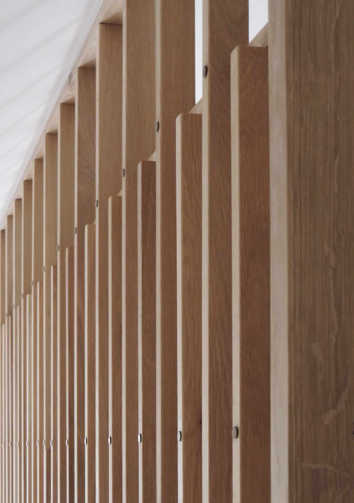 Detaliu al peretelui separator cu riflajul de lemn și ținte arămii ce fixează lamelele verticale