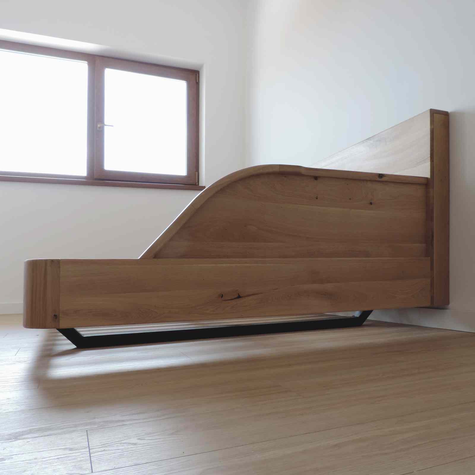 vedere din profil a patului recamier din stejar, cu piciorul metalic negru de dedesubt