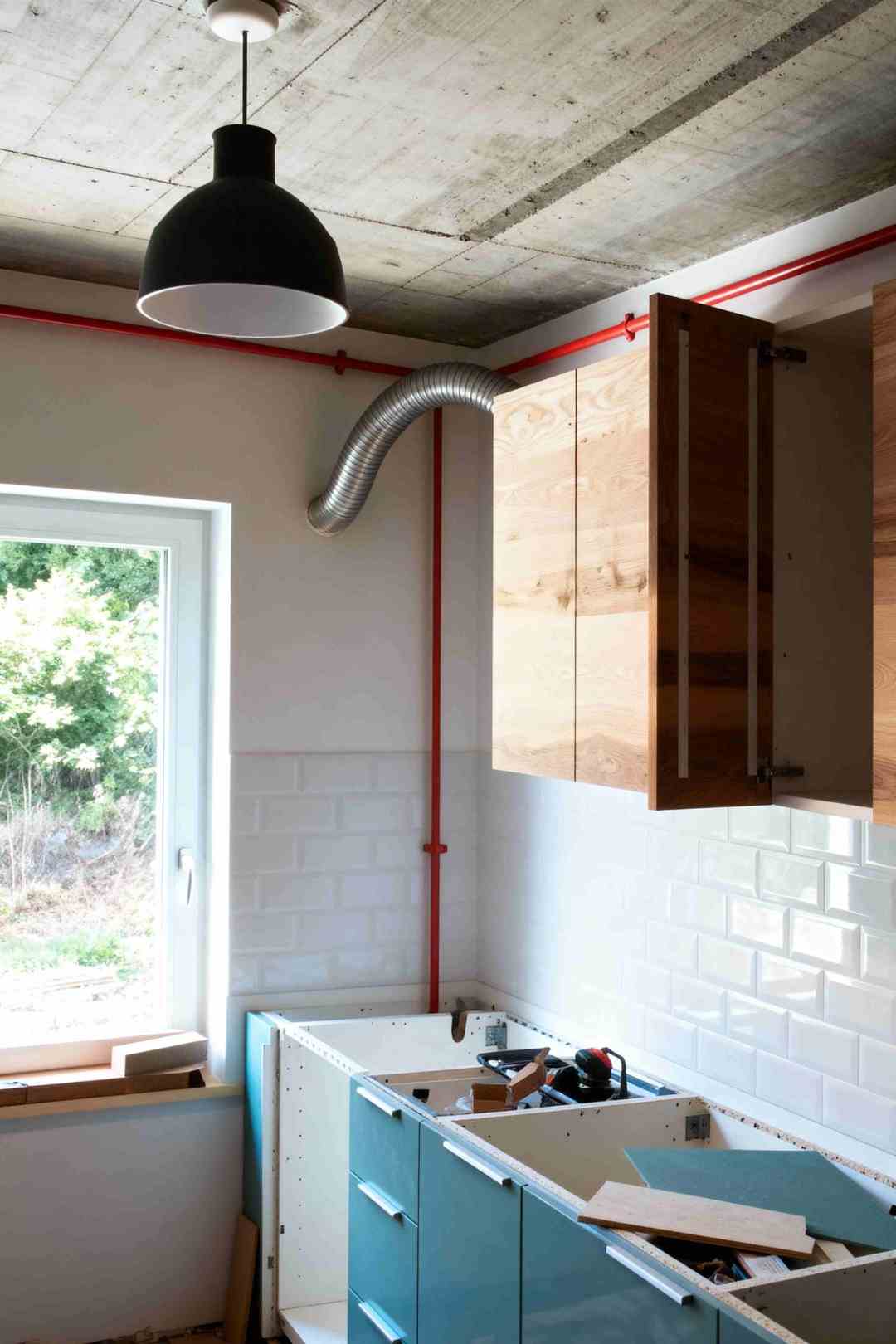 Imagine din timpul instalarii mobilierului de bucatarie cu dulapuri Ikea fara blat, cu usa din lemn de la partea superioara deschisa. Se observa unele unelte raspandite in mobila desfacuta.