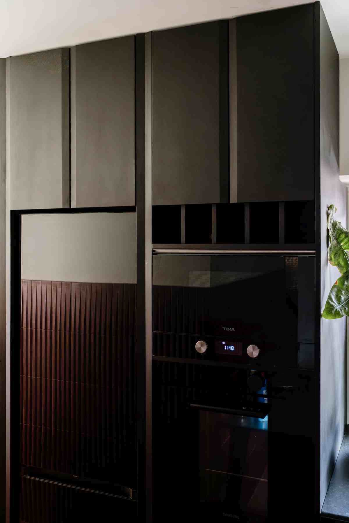 Dulap de bucatarie inalt de culoare neagra, cu frigider incorporat si cuptoare suprapuse negre. Usile superioare sunt de culoare negru mat cu profil tesit si suport de sticle inclus in mobilier